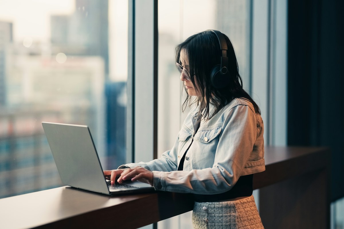 A woman working on a laptop at a high office window over a city