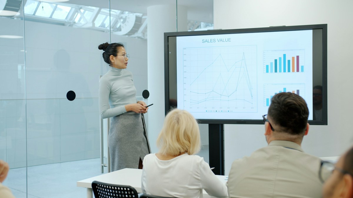 A woman presenting charts on a large screen to colleagues at a meeting table
