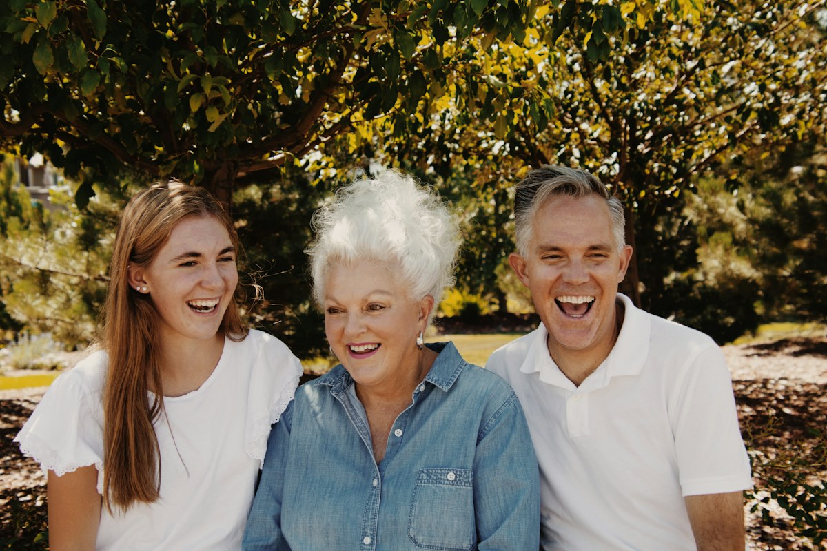 Three generations of a family laughing together outdoors in the sun